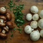 A side-by-side comparison of fresh crimini mushrooms and white mushrooms on a wooden cutting board. Crimini mushrooms are darker with firm caps, while white mushrooms are light and delicate. Natural lighting with an earthy kitchen setting in the background.