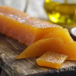 Whole and sliced bottarga on a wooden cutting board with olive oil and lemon.