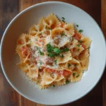 A delicious plate of Farfalle pasta coated in a rich, creamy sauce, garnished with fresh basil and grated Parmesan, served on a rustic wooden table.