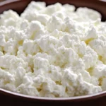 A bowl of fresh cottage cheese with visible whey separation.